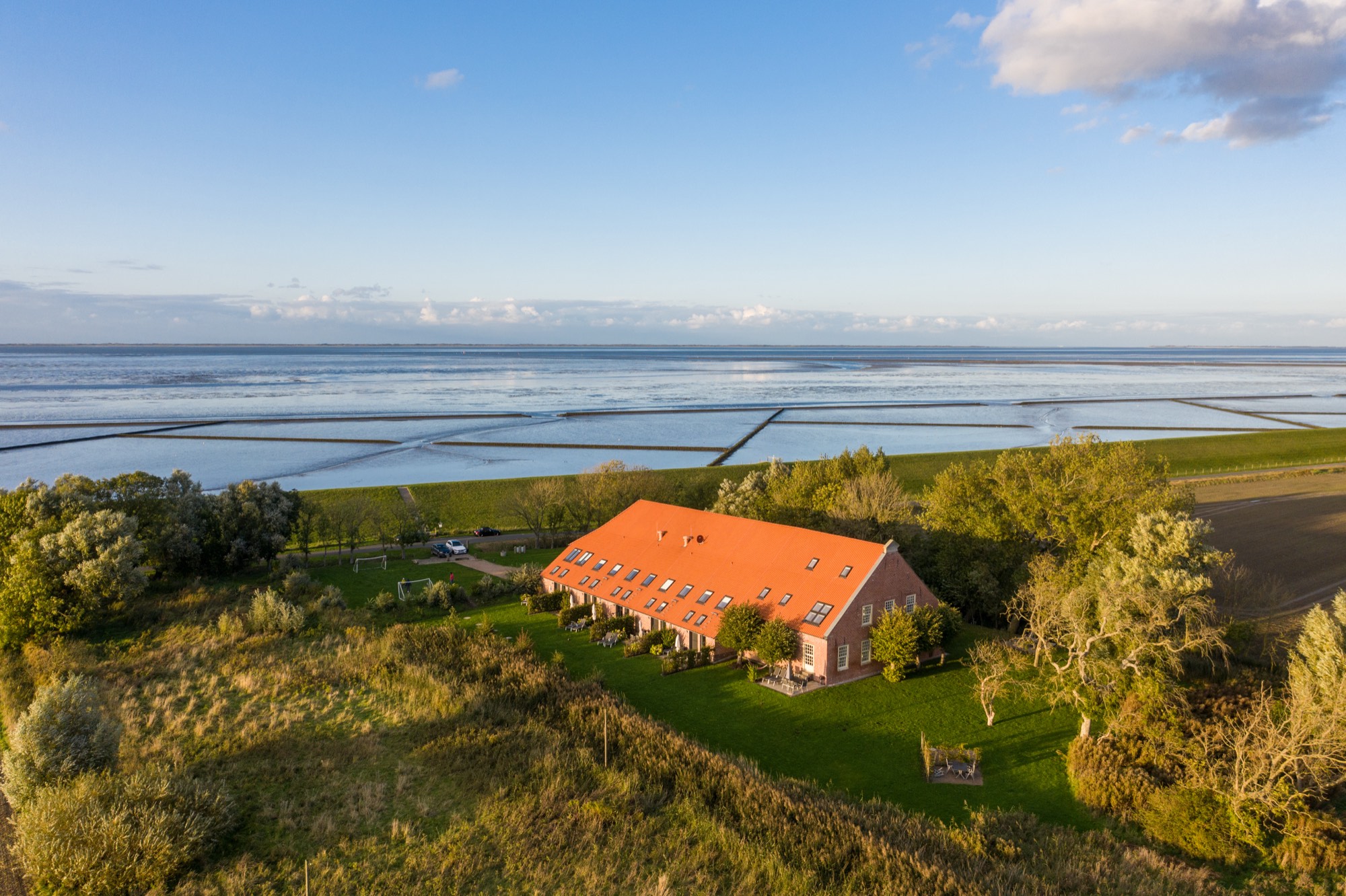 Luftaufnahme: der Gulfhof in Alleinlage direkt hinter dem Nordseedeich, dahinter das Wattenmeer